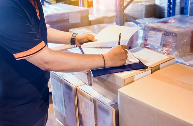Worker writing on notepad in shipping facility
