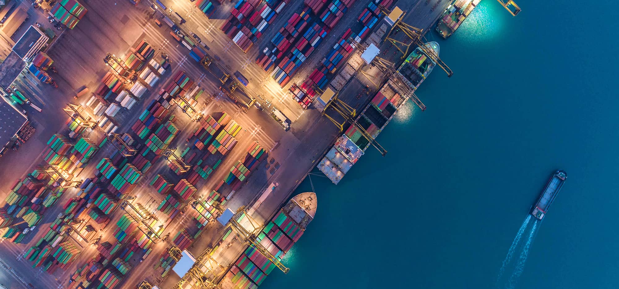 Aerial view of shipping container port with one ship cruising off shore in the ocean